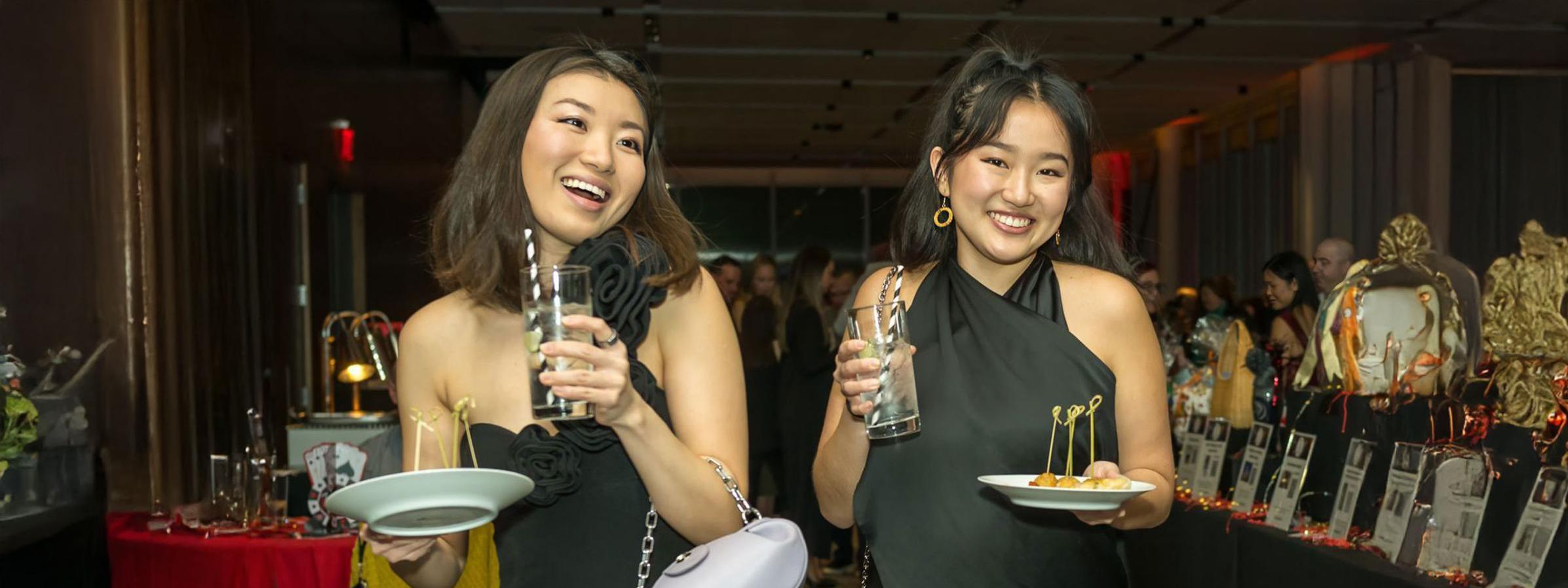 Two young women enjoying drinks and appetizers at a gala event