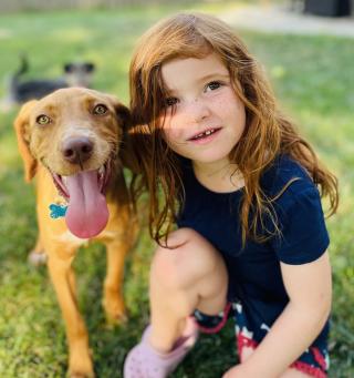 Girl kneeling next to a mixed breed dog.
