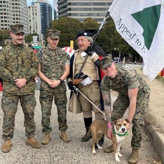A group of men in military uniforms with a lucky dog, and a man in a revolutionary army uniform