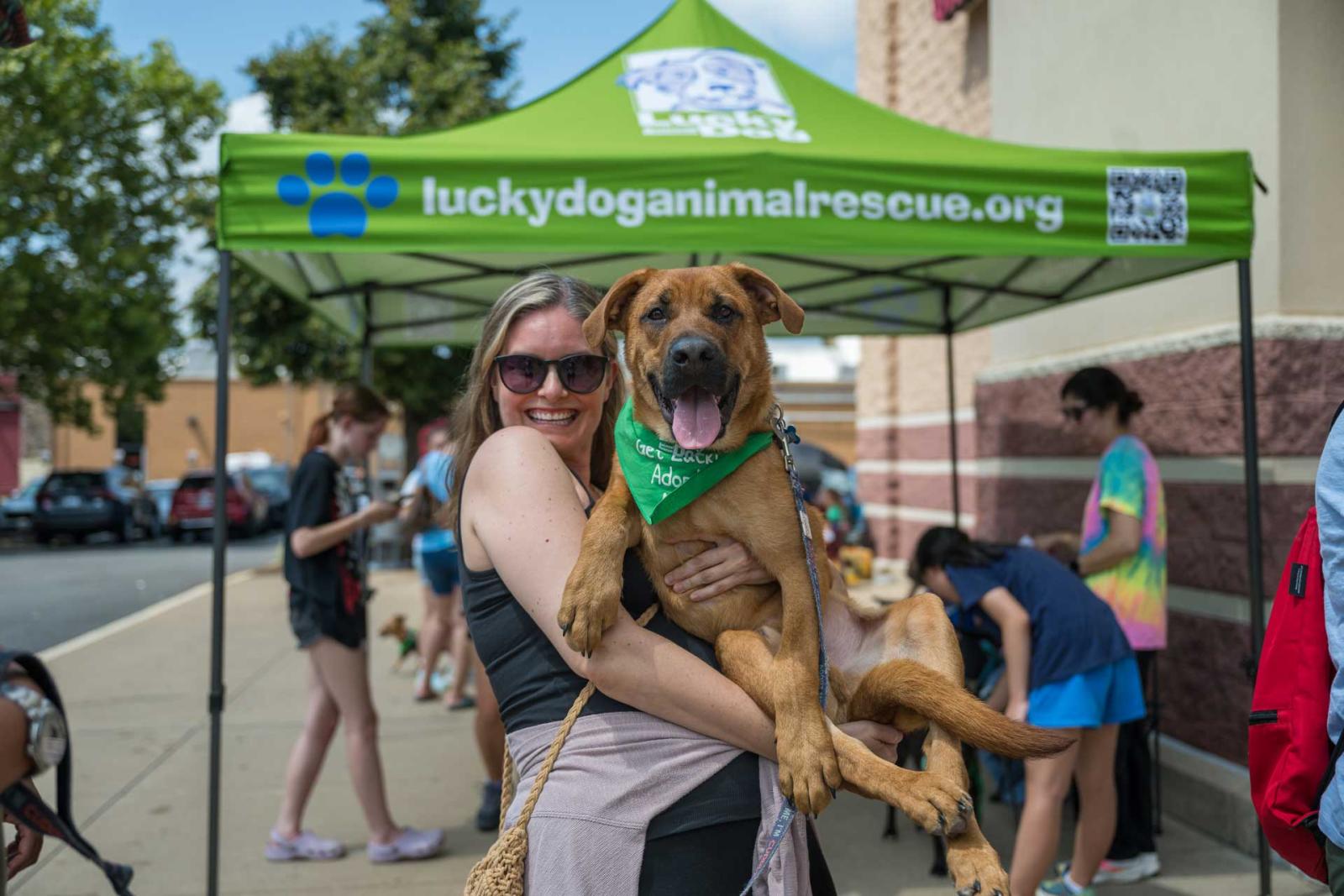 Woman holding large dog in front of an adoption booth.